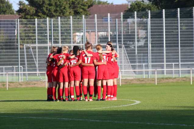 Frauenfu&szlig;ballmannschaft in roten Trikots umarmt sich auf dem Spielfeld vor dem Spiel.