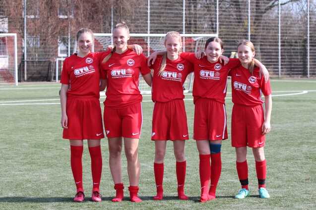 F&uuml;nf M&auml;dchen in roten Fu&szlig;balltrikots posieren gemeinsam auf einem Fu&szlig;ballfeld.