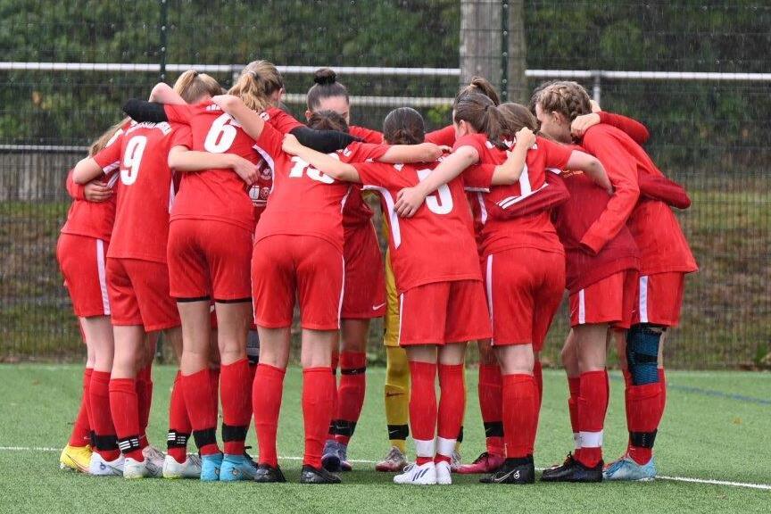 Eine Gruppe von 12 Fu&szlig;ballspielerinnen in roten Trikots steht im Kreis und h&auml;lt sich an den Schultern.