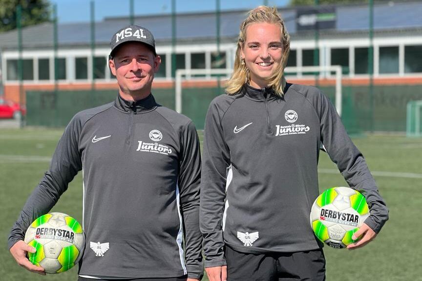 Zwei Personen in Sportkleidung halten jeweils einen Fu&szlig;ball auf einem gr&uuml;nen Fu&szlig;ballfeld.