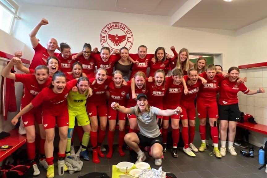 Gruppenfoto von Fu&szlig;ballspielerinnen in roten Trikots, die jubelnd in einem Umkleideraum stehen.