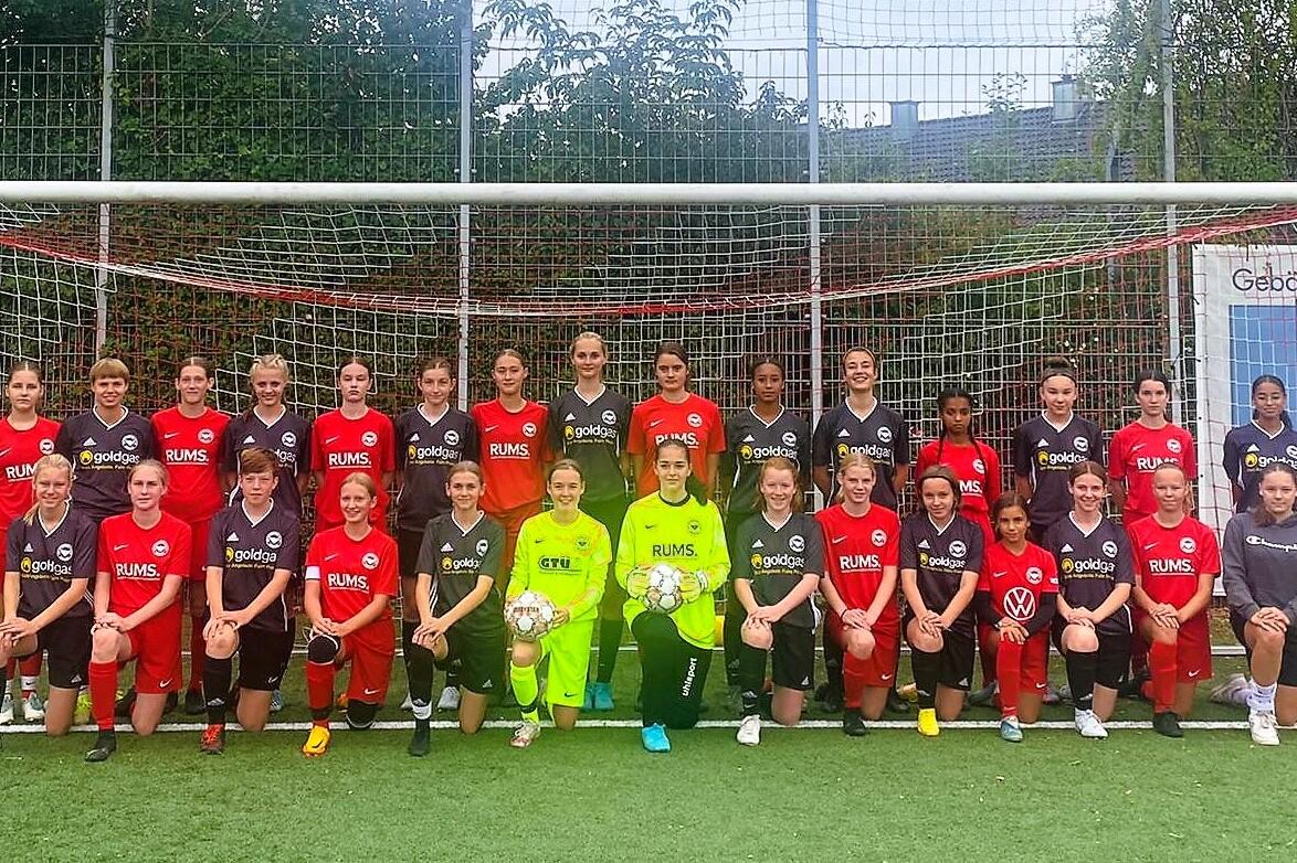 Gruppenfoto einer M&auml;dchenfu&szlig;ballmannschaft, bestehend aus 24 Spielerinnen in roten und schwarzen Trikots, vor einem Tor.