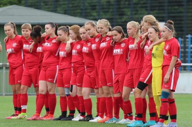 Gruppenszene von Frauenfu&szlig;ballerinnen in roten Trikots, auf einem Spielfeld, stehen nebeneinander vor einem Spiel.