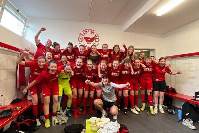 Gruppenfoto von Fu&szlig;ballspielerinnen in roten Trikots, die jubelnd in einem Umkleideraum stehen.