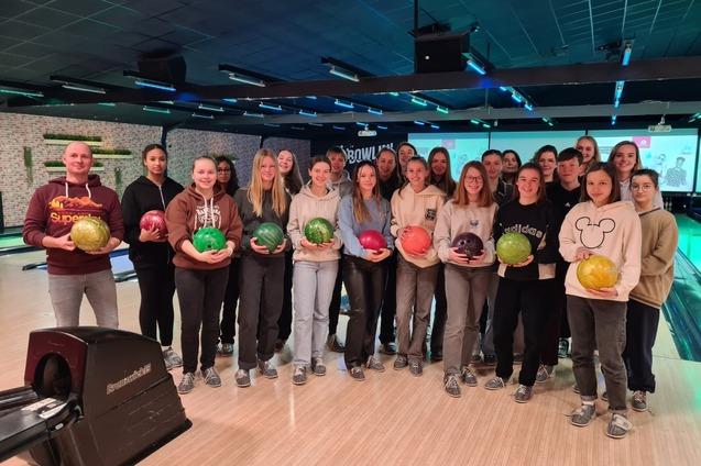Gruppencollage von 20 Personen in einem Bowling-Center, jede mit einer bunten Bowlingkugel in der Hand.