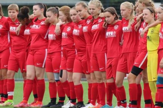 Gruppenszene von Frauenfu&szlig;ballerinnen in roten Trikots, auf einem Spielfeld, stehen nebeneinander vor einem Spiel.