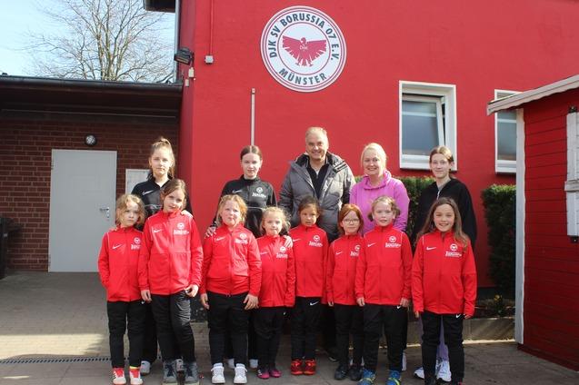 Gruppe von M&auml;dchen in roten Sportjacken vor einem Vereinsgeb&auml;ude mit dem Logo von Borussia M&uuml;nster.