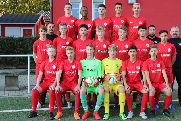 Gruppenfoto einer U16-Fu&szlig;ballmannschaft in roten Trikots, mit zwei Torh&uuml;tern und Fu&szlig;ballb&auml;llen auf einem Kunstrasenplatz.