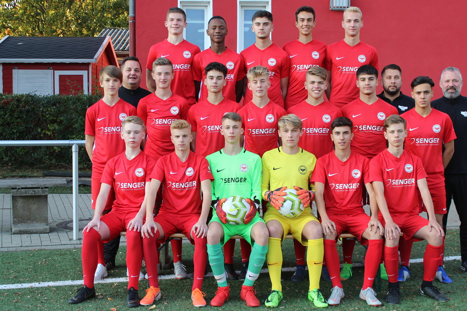 Gruppenfoto einer U16-Fu&szlig;ballmannschaft in roten Trikots, mit zwei Torh&uuml;tern und Fu&szlig;ballb&auml;llen auf einem Kunstrasenplatz.