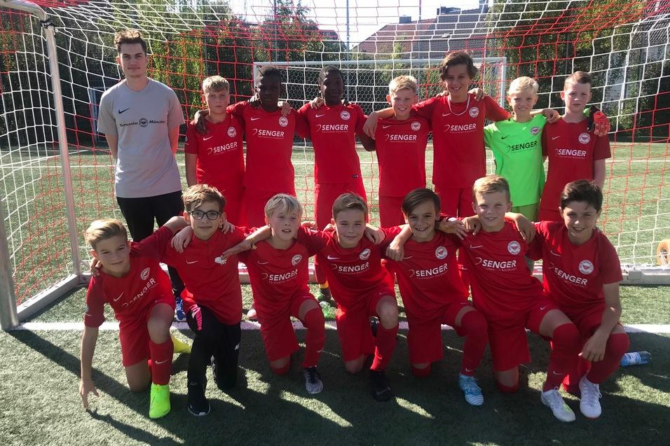 Gruppe von Fu&szlig;ballspielern in roten Trikots posiert vor einem Tor auf einem Sportplatz.