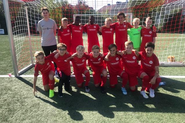Gruppe von Fu&szlig;ballspielern in roten Trikots posiert vor einem Tor auf einem Sportplatz.