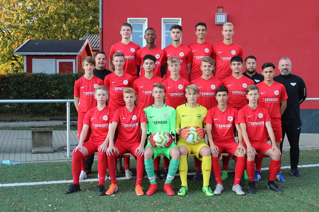 Gruppenfoto einer U16-Fu&szlig;ballmannschaft in roten Trikots, mit zwei Torh&uuml;tern und Fu&szlig;ballb&auml;llen auf einem Kunstrasenplatz.