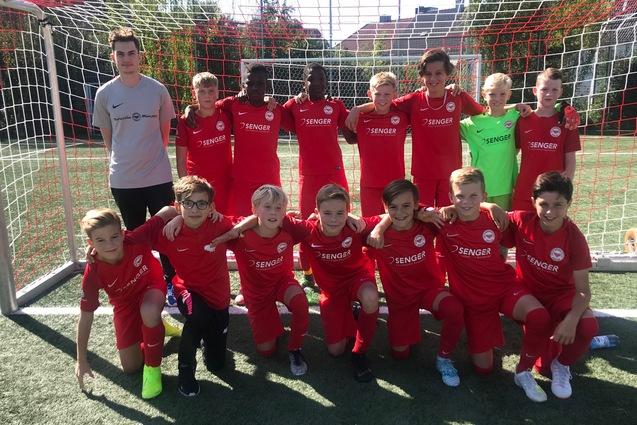 Gruppe von Fu&szlig;ballspielern in roten Trikots posiert vor einem Tor auf einem Sportplatz.