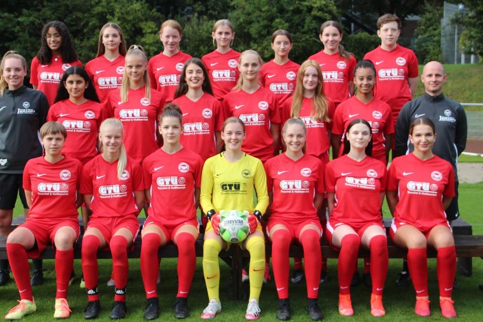 Frauenfu&szlig;ballmannschaft in roten Trikots posiert auf einer Bank auf einem Sportplatz, Torwart mit Ball in der Mitte.