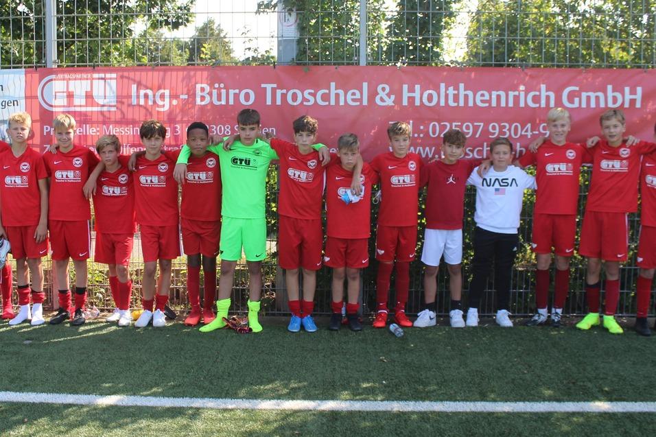 Gruppe von Fu&szlig;ballspielern in roten Trikots posiert auf einem Sportplatz mit Werbebanner im Hintergrund.