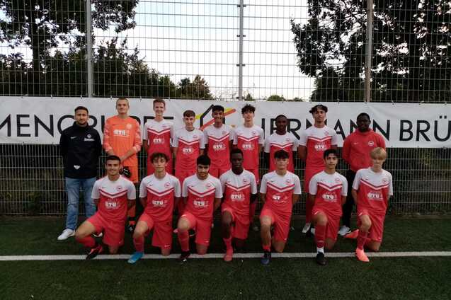 Gruppenfoto einer Jugendfu&szlig;ballmannschaft in roten Trikots auf einem Sportplatz, mit Trainer und Torwart.