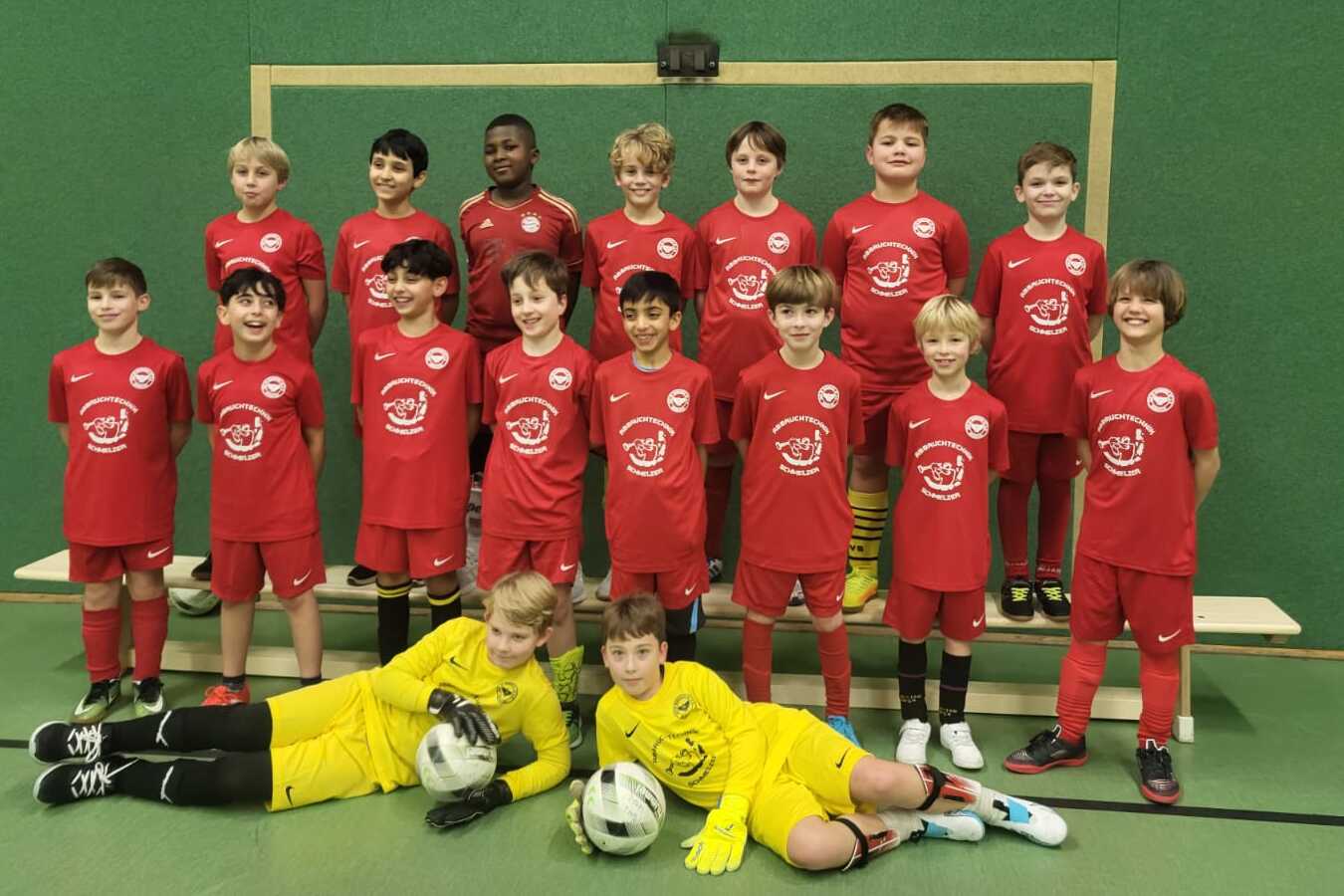 Gruppenupload von jungen Fu&szlig;ballspielern in roten Trikots, inklusive Torwart im gelben Trikot, vor einem Tor.