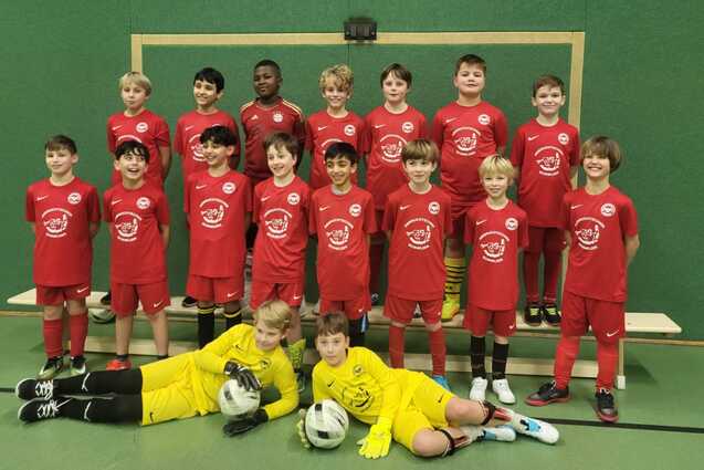 Gruppenupload von jungen Fu&szlig;ballspielern in roten Trikots, inklusive Torwart im gelben Trikot, vor einem Tor.