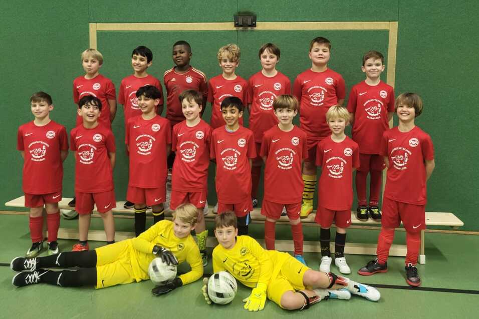 Gruppenupload von jungen Fu&szlig;ballspielern in roten Trikots, inklusive Torwart im gelben Trikot, vor einem Tor.