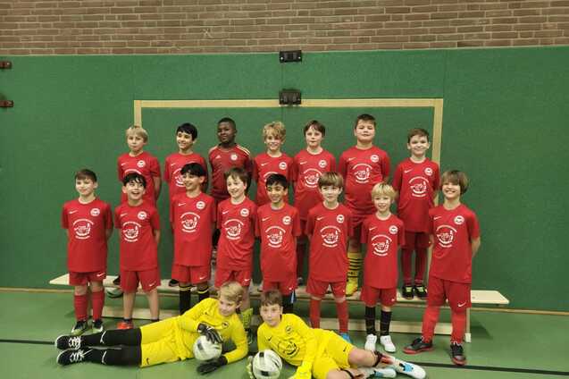 Gruppenupload von jungen Fu&szlig;ballspielern in roten Trikots, inklusive Torwart im gelben Trikot, vor einem Tor.
