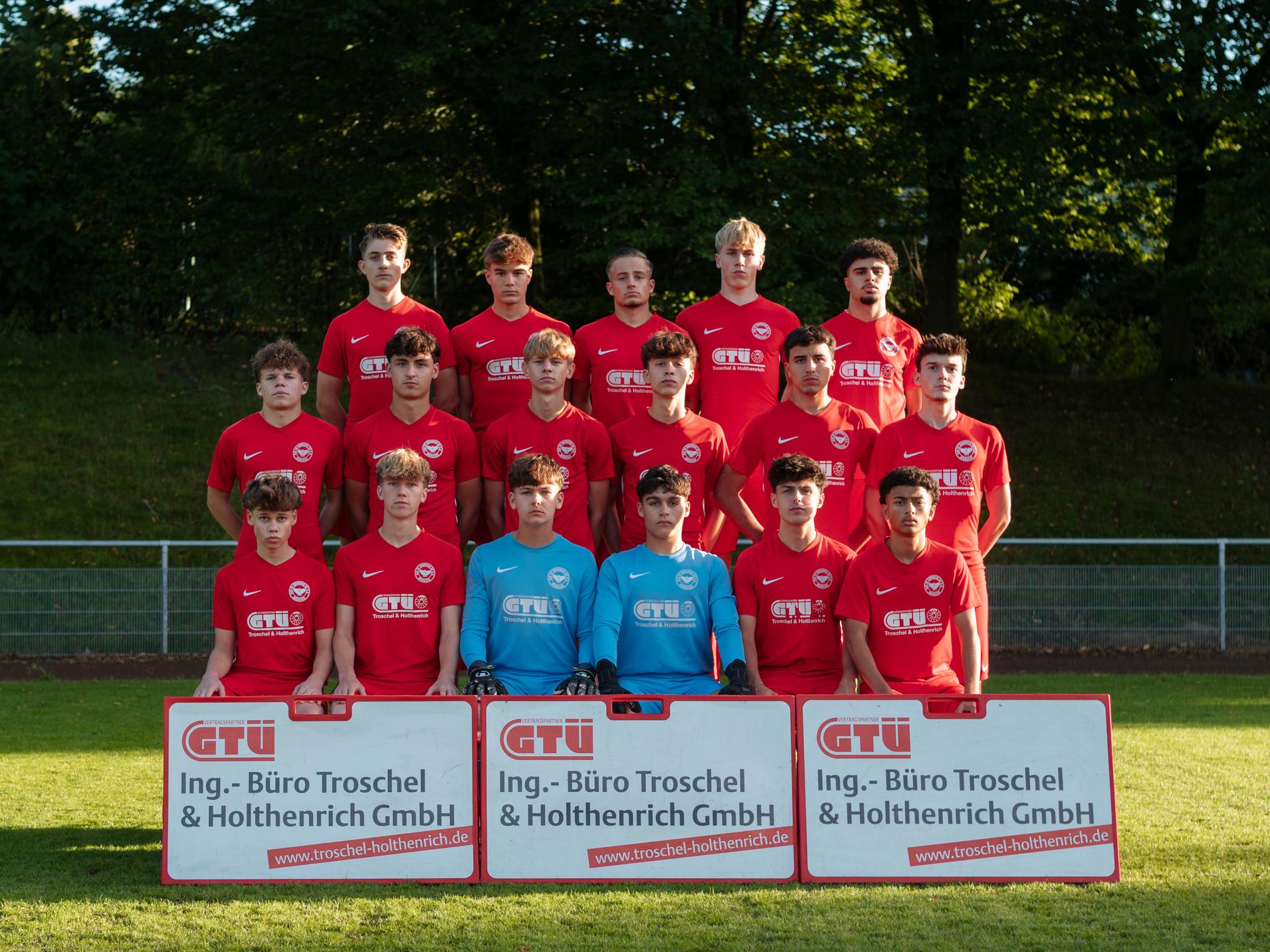 Mannschaftsfoto einer Jugendfu&szlig;ballmannschaft in roten Trikots mit Torwart, zwei Sponsorenbannern im Vordergrund.