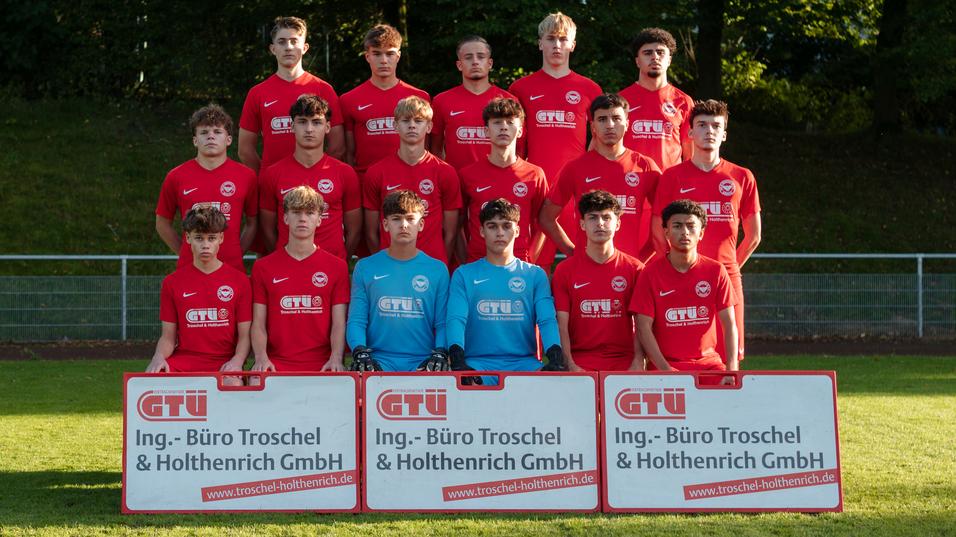 Mannschaftsfoto einer Jugendfu&szlig;ballmannschaft in roten Trikots mit Torwart, zwei Sponsorenbannern im Vordergrund.