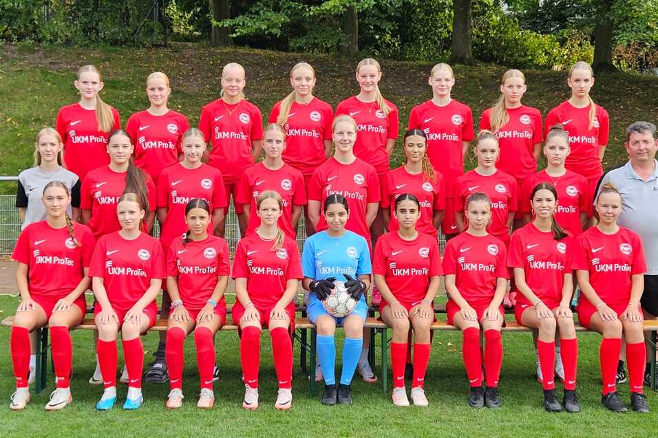 Mannschaftsfoto einer Fu&szlig;ballmannschaft mit 20 Spielerinnen in roten Trikots und einem Trainer auf einer Wiese.