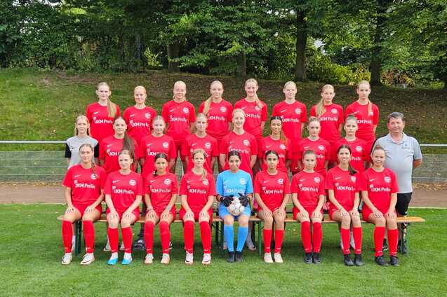 Mannschaftsfoto einer Fu&szlig;ballmannschaft mit 20 Spielerinnen in roten Trikots und einem Trainer auf einer Wiese.