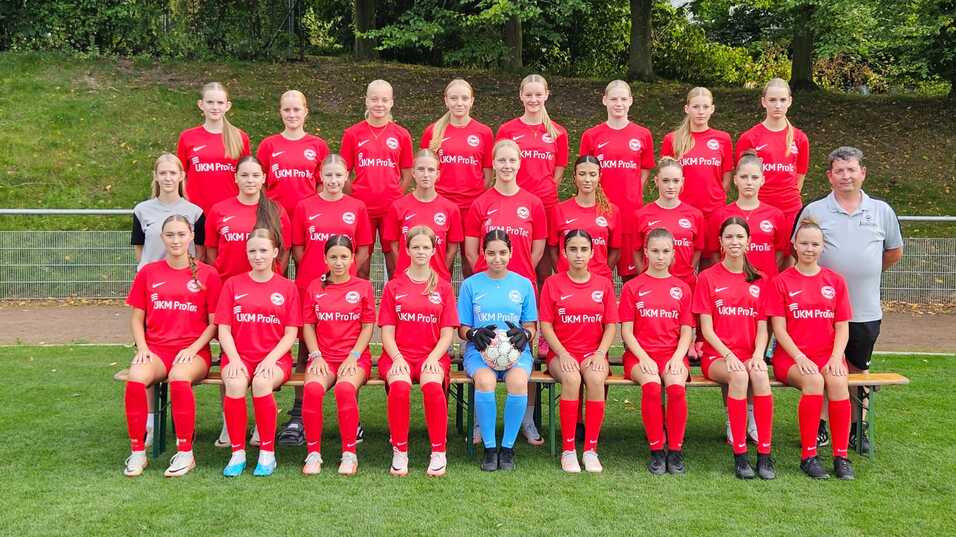 Mannschaftsfoto einer Fu&szlig;ballmannschaft mit 20 Spielerinnen in roten Trikots und einem Trainer auf einer Wiese.
