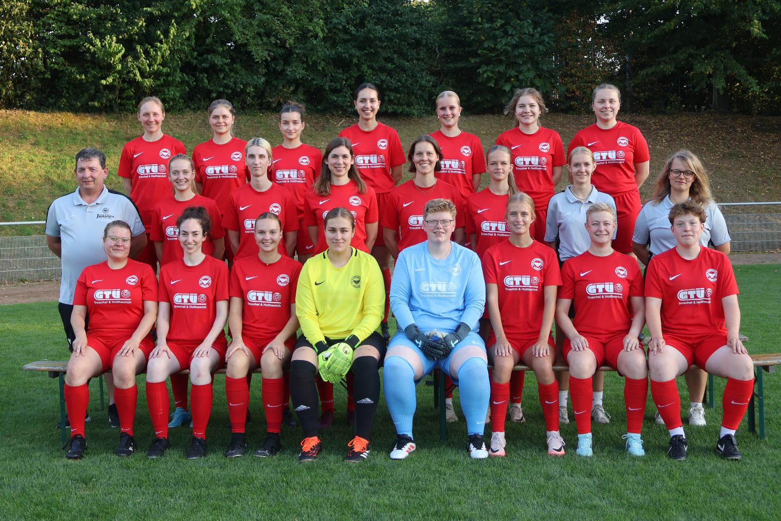 Mannschaftsfoto einer Damenfu&szlig;ballmannschaft in roten Trikots, gruppiert auf einer Wiese.