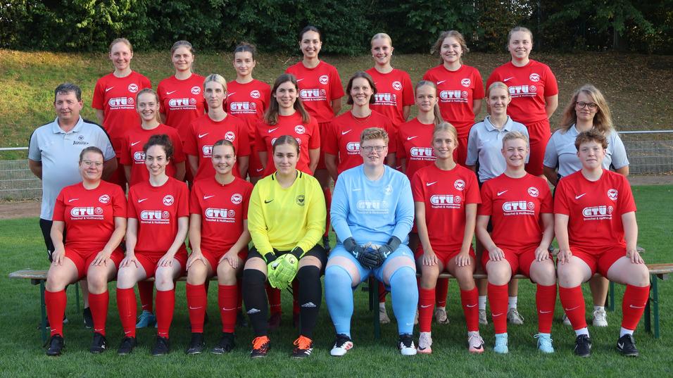 Mannschaftsfoto einer Damenfu&szlig;ballmannschaft in roten Trikots, gruppiert auf einer Wiese.