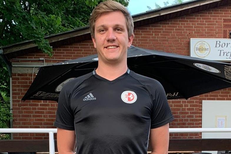 Junger Mann in schwarzem Fu&szlig;balltrikot steht vor einem Geb&auml;ude mit der Aufschrift "Borussen Treffler".