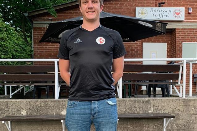 Junger Mann in schwarzem Fu&szlig;balltrikot steht vor einem Geb&auml;ude mit der Aufschrift "Borussen Treffler".