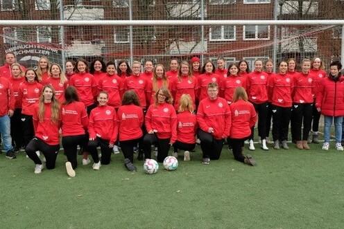 Gruppenfoto von Frauenfu&szlig;ballspielern in roten Trainingsjacken, stehend und sitzend vor einem Fu&szlig;balltor.