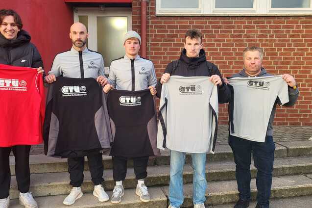 F&uuml;nf Personen stehen auf einer Treppe und halten verschiedene T-Shirts mit dem Logo &bdquo;GTU&ldquo; in schwarz, rot und grau.