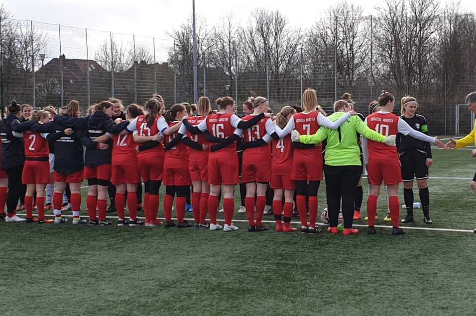 Zwei Gruppen von Fu&szlig;ballerinnen in rot und schwarz stehen sich auf einem Kunstrasenfeld gegen&uuml;ber und begr&uuml;&szlig;en sich.