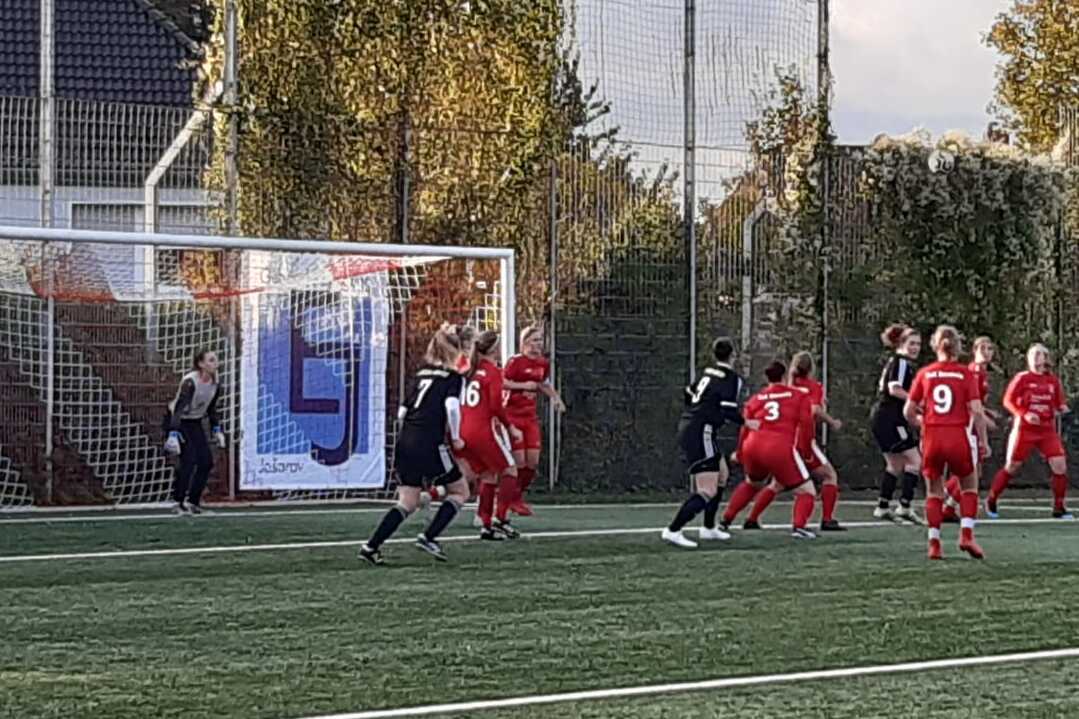 Fu&szlig;ballspiel mit Spielern in roten und schwarzen Trikots vor dem Tor auf einem Kunstrasenplatz.
