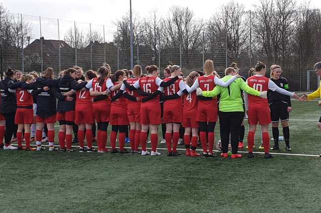 Zwei Gruppen von Fu&szlig;ballerinnen in rot und schwarz stehen sich auf einem Kunstrasenfeld gegen&uuml;ber und begr&uuml;&szlig;en sich.