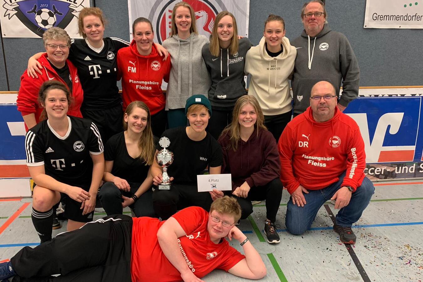 Gruppenfoto von Frauenmannschaft mit Pokal und Urkunde in Sportkleidung in einer Halle. Im Hintergrund Vereinsbanner sichtbar.