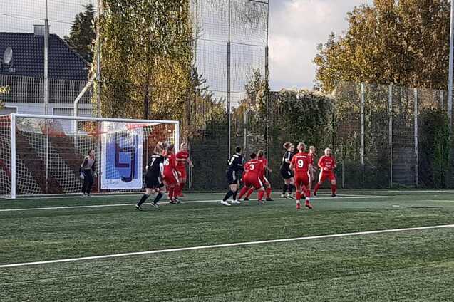Fu&szlig;ballspiel mit Spielern in roten und schwarzen Trikots vor dem Tor auf einem Kunstrasenplatz.