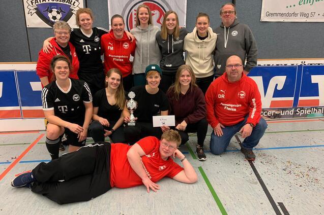 Gruppenfoto von Frauenmannschaft mit Pokal und Urkunde in Sportkleidung in einer Halle. Im Hintergrund Vereinsbanner sichtbar.