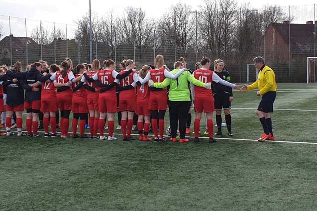 Zwei Gruppen von Fu&szlig;ballerinnen in rot und schwarz stehen sich auf einem Kunstrasenfeld gegen&uuml;ber und begr&uuml;&szlig;en sich.