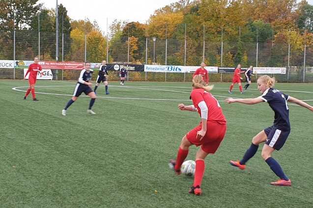 Zwei Fu&szlig;ballspielerinnen in roten und blauen Trikots k&auml;mpfen um den Ball auf einem Kunstrasenplatz.