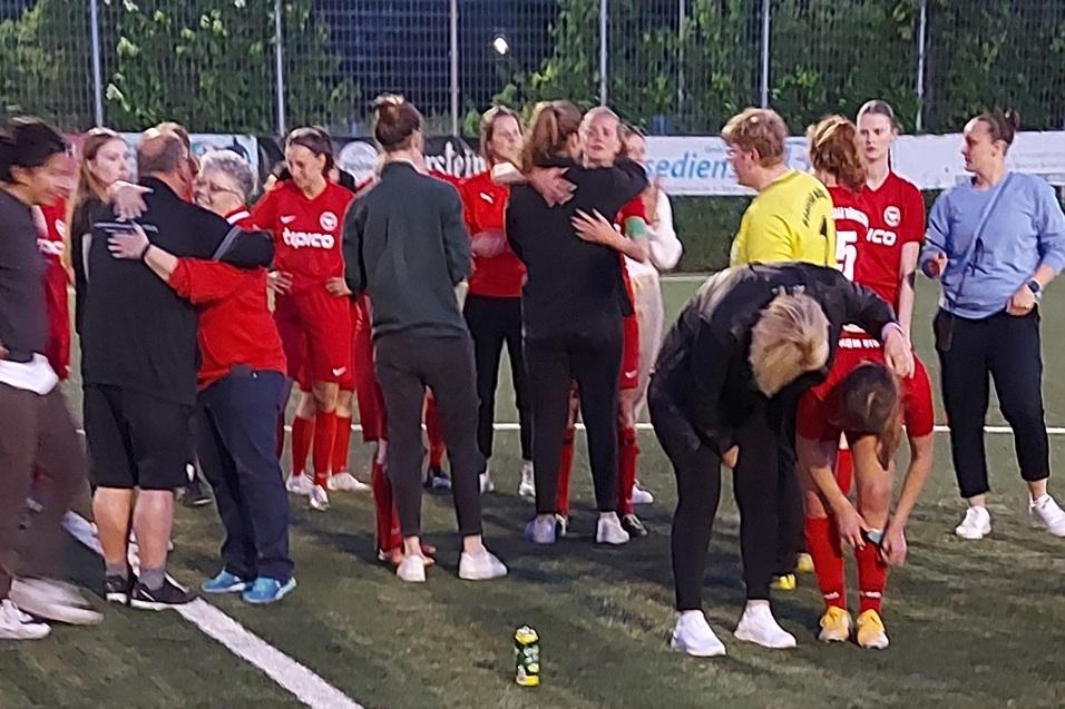Gruppenszene von Fu&szlig;ballspielerinnen in roten Trikots, die sich auf einem Platz umarmen und feiern.