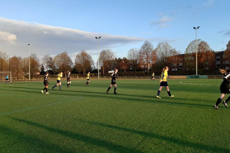 Spielszene auf einem Fu&szlig;ballplatz mit Spielern in gelben und schwarzen Trikots unter blauem Himmel und herbstlichen B&auml;umen.