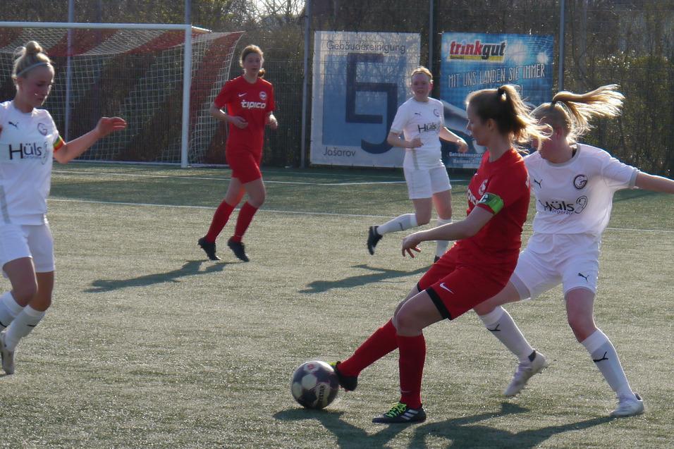 Zwei Fu&szlig;ballspielerinnen in roten und wei&szlig;en Trikots k&auml;mpfen um den Ball auf einem Kunstrasenplatz.