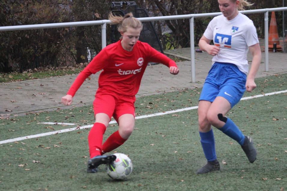 Zwei Fu&szlig;ballspielerinnen im Wettkampf um den Ball auf einem Rasenfeld, eine in rotem und die andere in blau-wei&szlig;em Trikot.