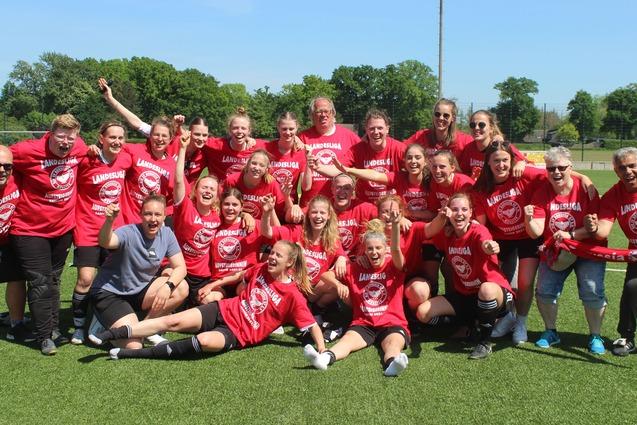 Gruppenshot eines begeisterten Frauenfu&szlig;ballteams in roten Shirts, das auf einem Platz feiert und jubelt.