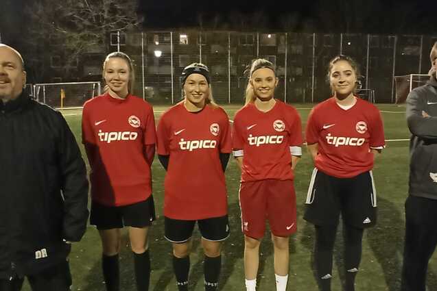 F&uuml;nf Fu&szlig;ballspielerinnen in roten Trikots stehen auf einem Sportplatz bei Nacht, zwei Trainer daneben.