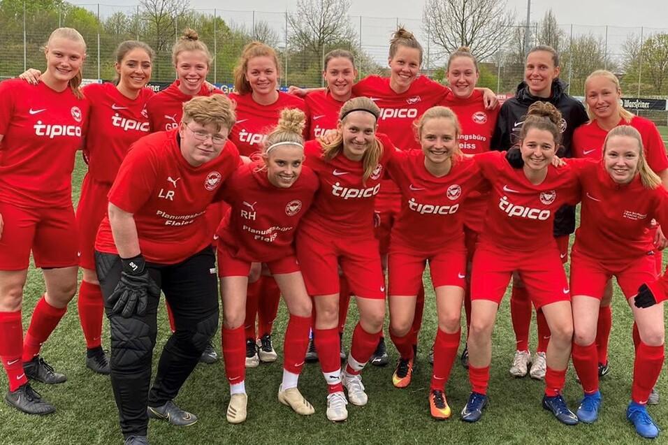 Gruppenfoto von 16 Fu&szlig;ballspielerinnen in roten Trikots auf einem Rasenplatz, smiling und in sportlicher Pose.